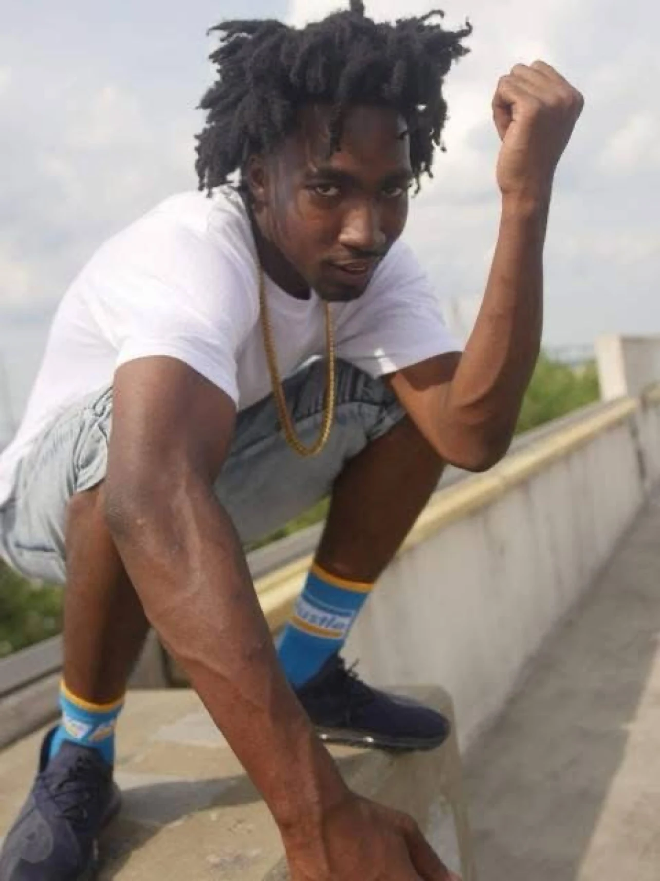 Keylo Da Beast crouching outdoors in a white shirt and gray shorts