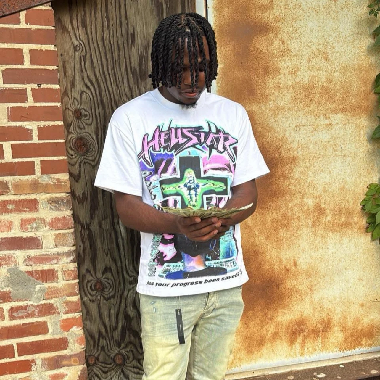 Lil5witch wearing a white graphic T-shirt and holding cash outdoors