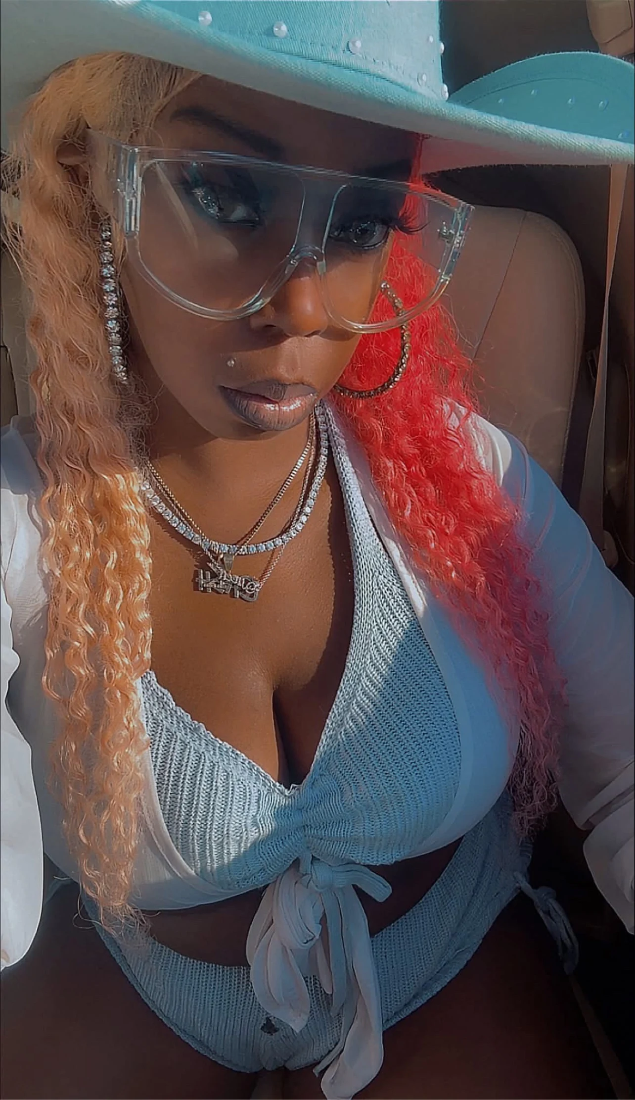 MillionDolla Ca$h taking a car selfie in a blue outfit and hat with multicolored hair