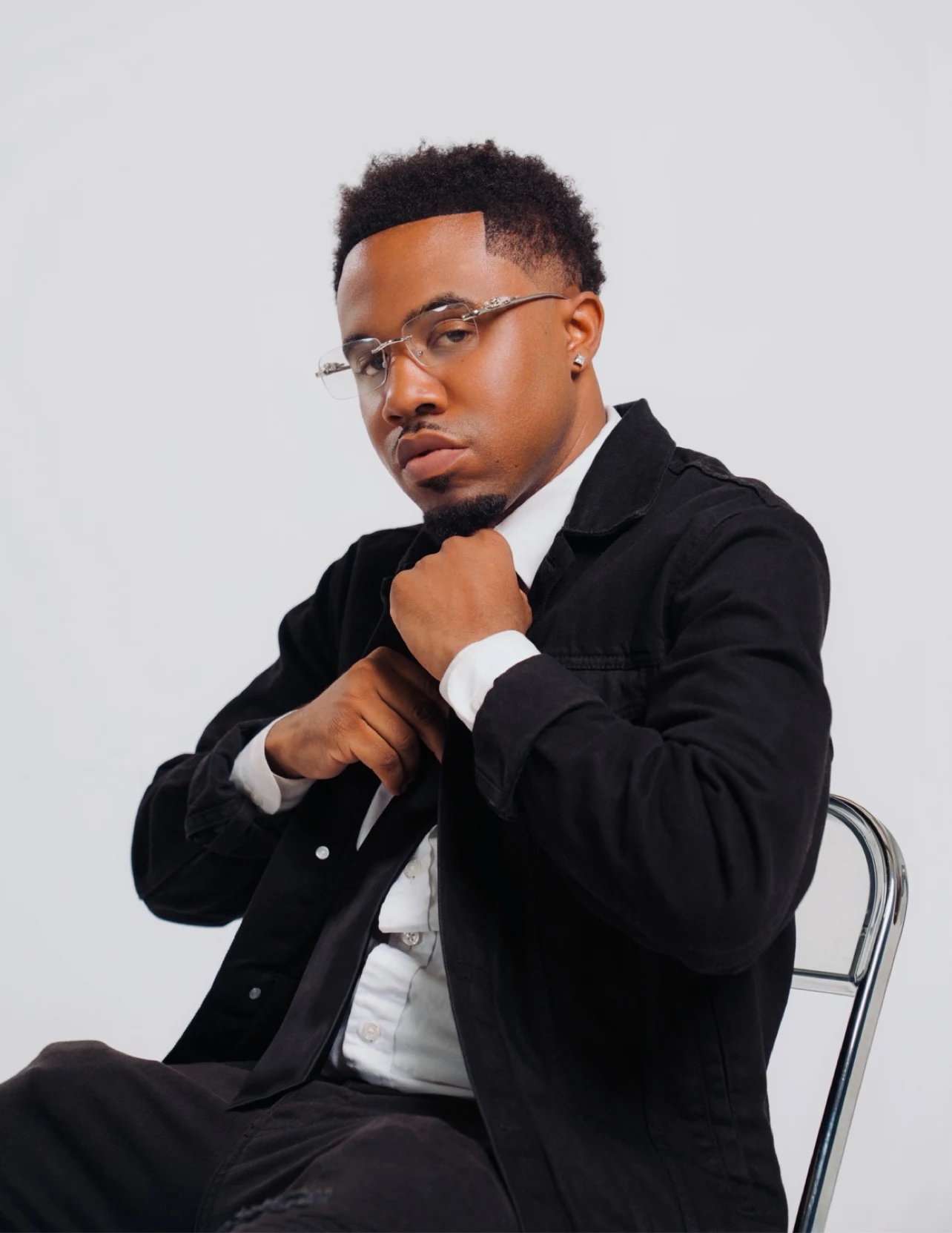 oNE Nuke seated in a black jacket and glasses for a studio portrait